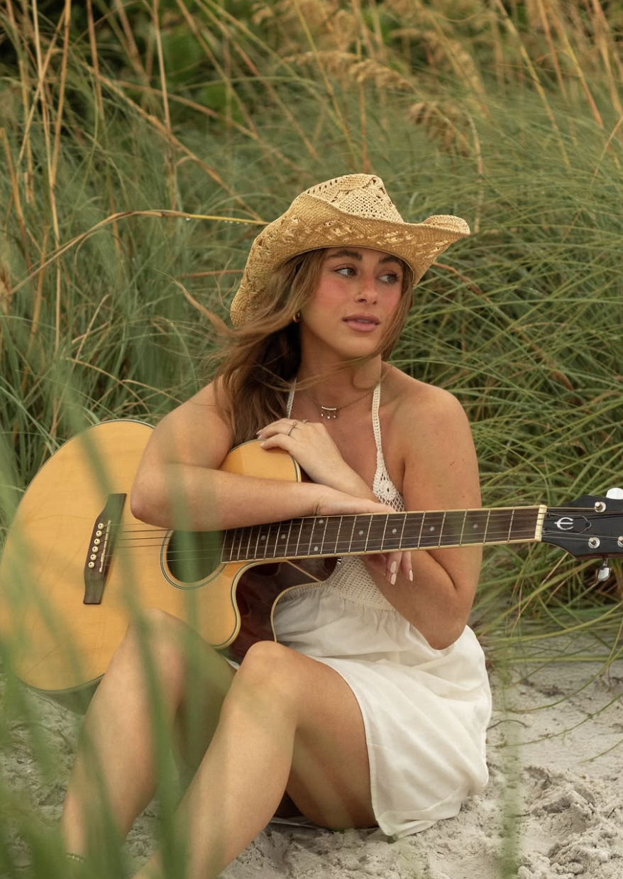 Leanne McGroary sitting on the beach with an acoustic guitar among sea grass